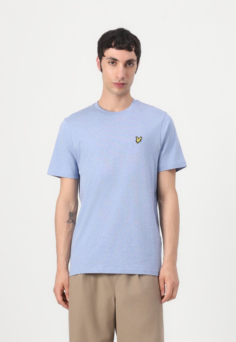 T-shirt bleu clair à manches courtes en coton doux avec un col rond et un petit logo jaune brodé sur la poitrine gauche.