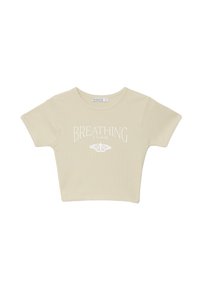 Camiseta corta de color beige claro con mangas cortas, que presenta el texto blanco "BREATHING" y un gráfico de mariposa. Está hecha de una tela suave y con canalé.