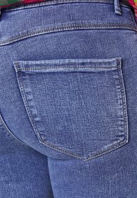 Jeans de ganga azuis com um bolso traseiro, costura visível e uma textura suave. O tecido apresenta um leve desgaste para um aspeto usado.