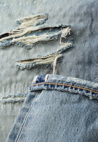 Blauwe denim stof met versleten gedeelten, met rafelige randen en een zichtbare tailleband met rode en blauwe stiksels.