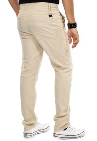 Beige leichte Hose mit geradem Schnitt, ausgestattet mit Gesäßtaschen und einer glatten Textur, kombiniert mit weißen Sneakers.