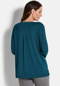 Türkisfarbener Langarm-Top mit einem gefalteten Rückendesign, rundem Ausschnitt und seitlichen Schlitzen. Hergestellt aus weich und glattem Material mit lässiger Passform.