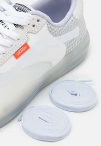 Sapatilha branca com detalhes em cinza e malha xadrez, atacadores brancos planos e um logótipo laranja da Vans. Inclui dois atacadores azul claro.