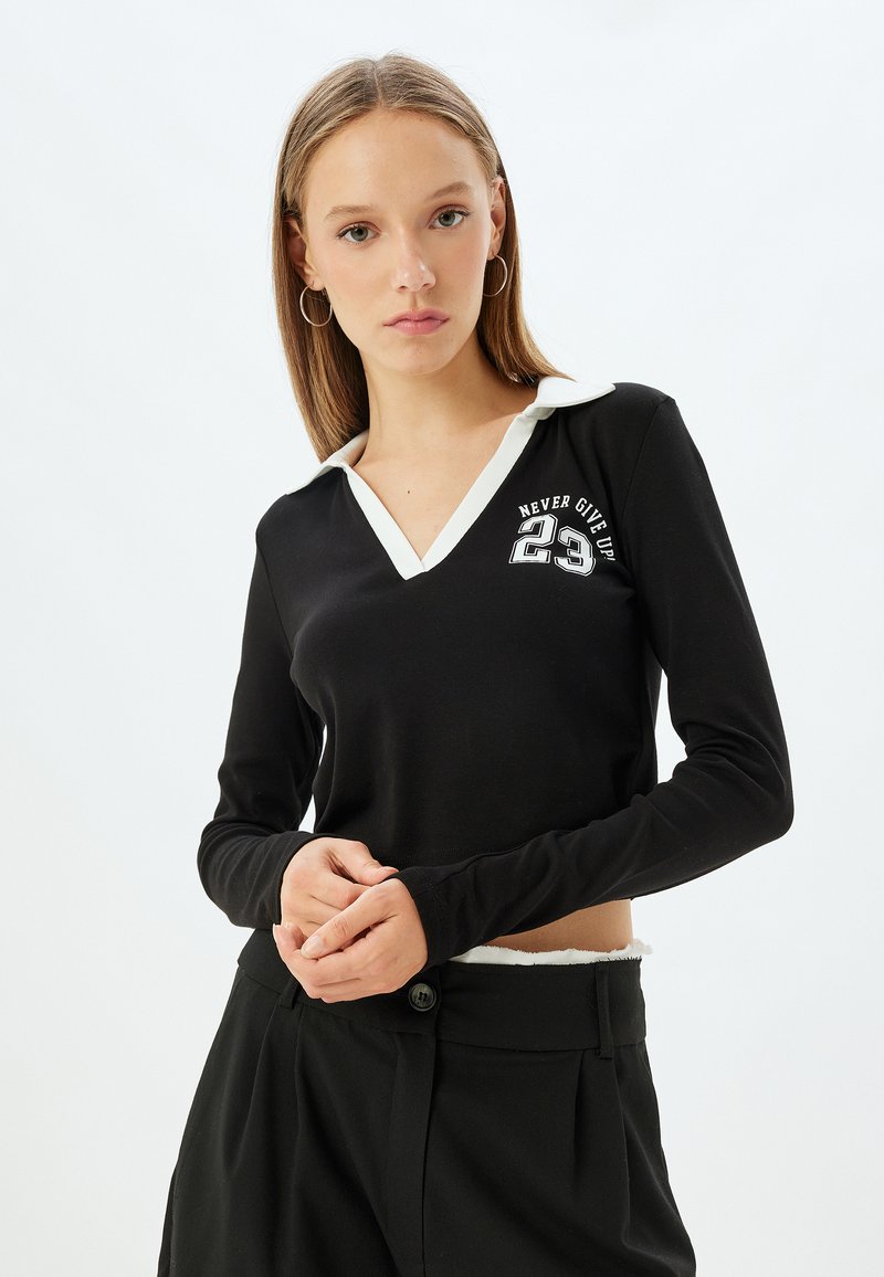 Mustat pitkät hihaiset paidat, joissa on valkoinen kaulus ja "NEVER GIVE UP 23" -grafiikka. Suunniltaan sujuva, istuva malli ja yksinkertaiset yksityiskohdat.
