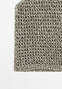 Gros plan d'un tissu beige et noir tricoté lâchement avec un motif ouvert et texturé et un ourlet tissé plus épais en bas.