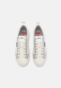 Białe i szare sneakersy z zamkiem sznurowym, z teksturowanej skóry i akcentami materiałowymi, z zakładką na pięcie i czerwonym logo na języku.