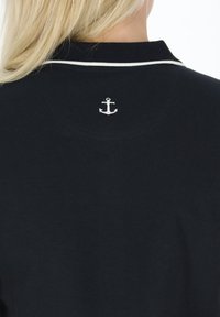 Marine polo-shirt med en hvid krave og et broderet ankerlogo på ryggen. Stoffet ser glat og struktureret ud.