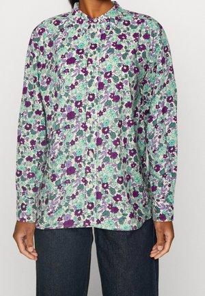 Overhemd met lange mouwen, knoopsluiting en een dicht bloemenpatroon in paars, groen en lavendel, gedragen met donkerblauwe spijkerbroek.
