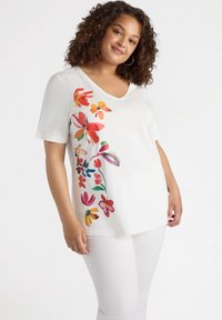 Camiseta blanca de manga corta con un colorido diseño floral en un lado. La tela es suave, con un escote en V y un corte relajado.