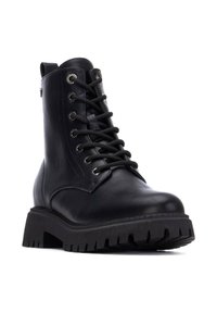 Stivaletto in pelle nera con lacci, occhielli in metallo argentato e suola spessa e testurizzata. Presenta un tassello sul retro.