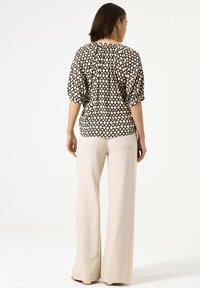 Blouse noire et crème à motifs avec des manches bouffantes, associé à un pantalon large beige. La blouse présente un détail froncé au dos.