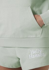 Sudadera de algodón verde claro con bolsillo tipo canguro, combinada con pantalones cortos a juego que presentan el logotipo bordado en blanco "Helly Hansen".