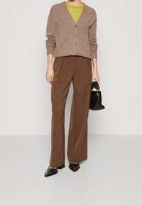 Brązowy kardigan z dekoltem w serek, beżowe guziki; w połączeniu z wysokim stanem brązowych spodni. Czarna torebka i czarne szpiczaste buty dopełniają stylizację.