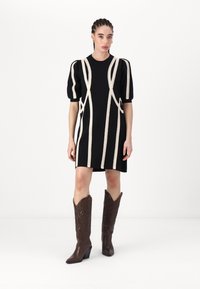 Zwarte gebreide jurk met witte kantdetails, poefmouwen en een korte zoom, gecombineerd met bruine cowboylaarzen met een spitse neus.