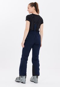 Blå skidbyxor med justerbara remmar, med en stilren design och elastisk midja. Tillsammans med grå skidstövlar och en figurnära svart topp.