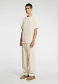 Beżowa bawełniana koszulka o luźnym kroju i krótkich rękawach, zestawiona z pasującymi beżowymi bawełnianymi spodniami i brązowymi zamszowymi butami.