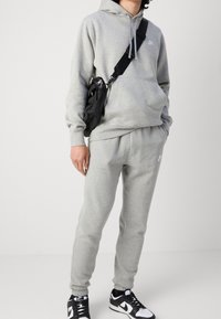 Grå huvtröja och joggingbyxor i mjukt tyg, med en liten logotyp. Kombinerat med svarta och vita sneakers samt en svart axelväska.