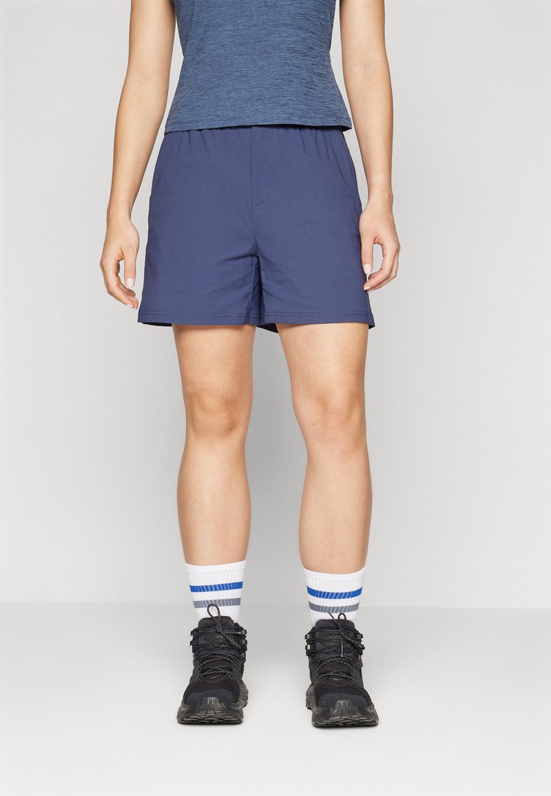 Mørkeblå shorts med elastisk talje, over knæ længde, parret med hvide sokker med blå striber og sorte vandrestøvler.