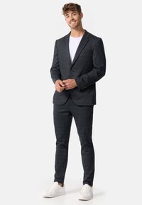 Traje de cuadros gris oscuro con un blazer de un solo botón, pantalones ajustados, combinado con una camiseta blanca y zapatillas blancas.