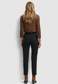 Blouse marron à motifs avec des manches trois-quarts, associée à un pantalon noir à rayures; le mannequin porte des bottines marron.