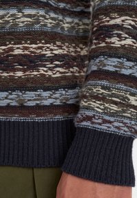 Strikket sweater med flerfarvet mønster, der viser mørkegrønne, blå, cremefarvede og maroon striber. Ribbet manchet i marineblå ved håndleddet.