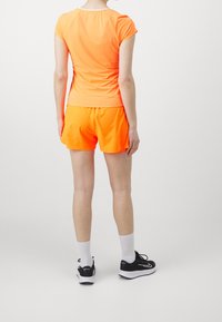 Oranssi urheilupaita ja siihen sopivat shortsit, joissa on sileä pinta, yhdistettynä mustiin lenkkareihin ja valkoisiin nilkkasukkiin.