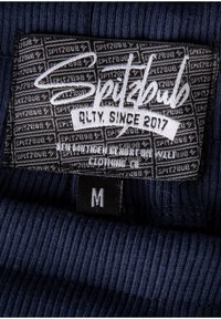 Navy ribbed fabric label featuring "Spitzbub" in white script, size tag 'M,' with a textured black background and pattern.