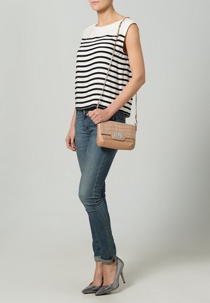 Mujer con top sin mangas a rayas, vaqueros ajustados, tacones altos metálicos y un bolso beige de bandolera con cadena.