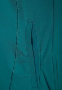 Tyrkysová strečová tkanina s diskrétním bočním kapsou s plochým otvorem, úhledným švem a hladkou strukturou.