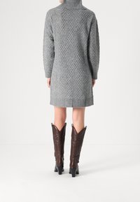 Šedé pletené svetrové šaty s rolákem, zdobené texturovaným diamantovým vzorem, s žebrovaným lemem a dlouhými rukávy, doplněné hnědými kovbojskými botami.