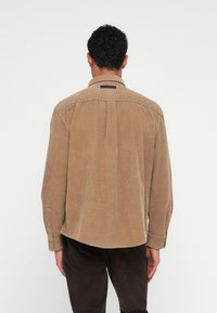 Bruine corduroy overhemd met een ontspannen pasvorm, met een rugplooi, knooploze manchetten en een klein label op de bovenrug.