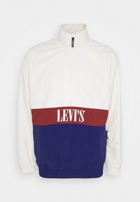 Džísová bunda Levi's s bílou horní částí, vínovým středovým pruhem a modrým spodním dílem, s polovičním zipem a elastickými manžetami.