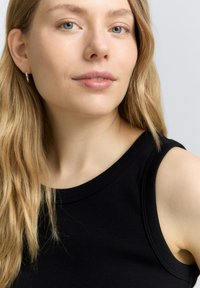 Top sin mangas negro con cuello redondo, que presenta detalles de costura mínimos y una textura suave. La modelo tiene el cabello claro y la piel clara.