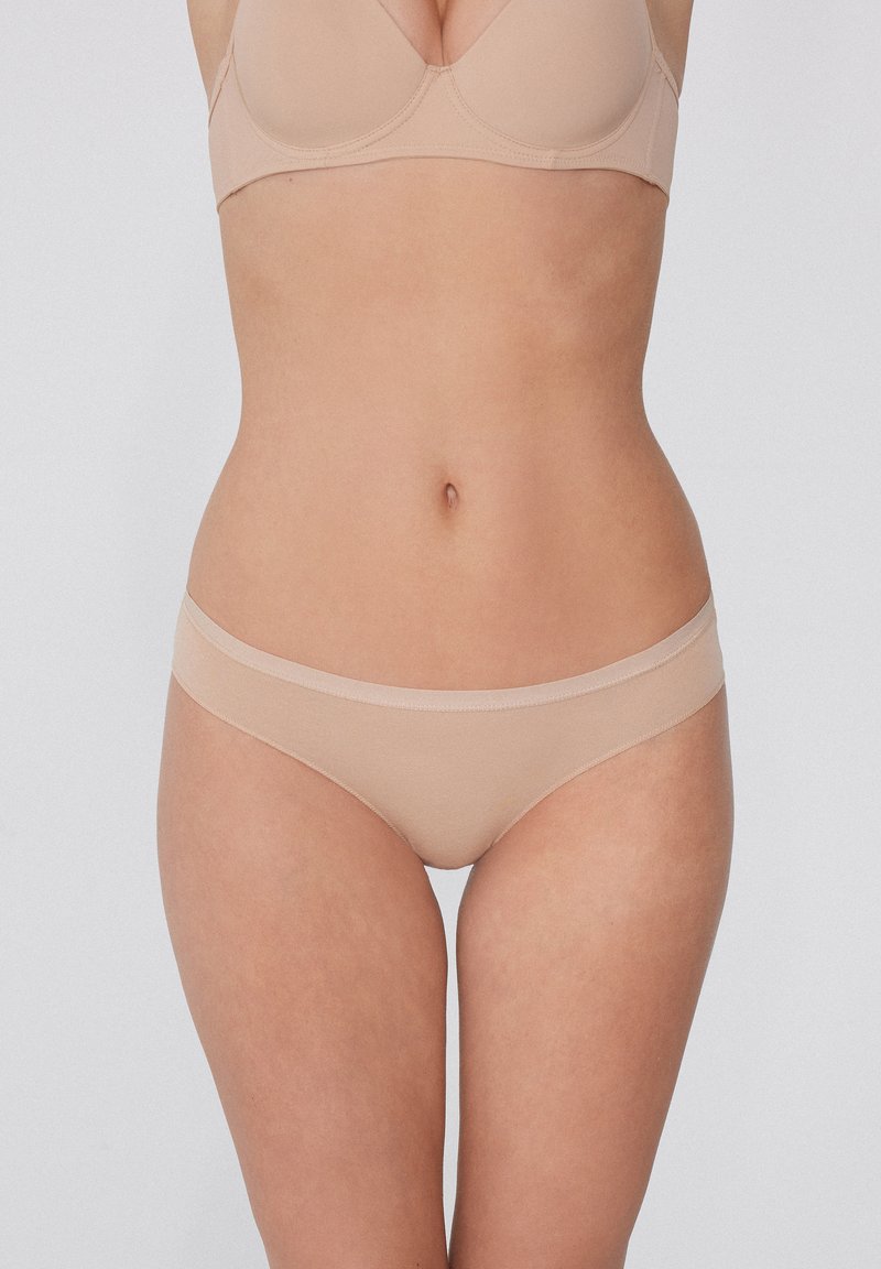 Béžové spodní prádlo se hladkým, bezešvým designem, jemným elastickým páskem a minimálním pokrytím, vyrobené z lehkého materiálu.