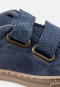 Navy blue suede sneaker with two velcro straps and bronze grommets, featuring a textured surface and a beige rubber sole.