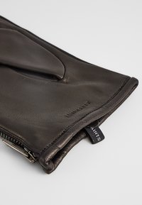 Guanto in pelle nera con una superficie liscia, dotato di una chiusura con zip e di un piccolo cartellino del marchio visibile vicino alla cucitura laterale.
