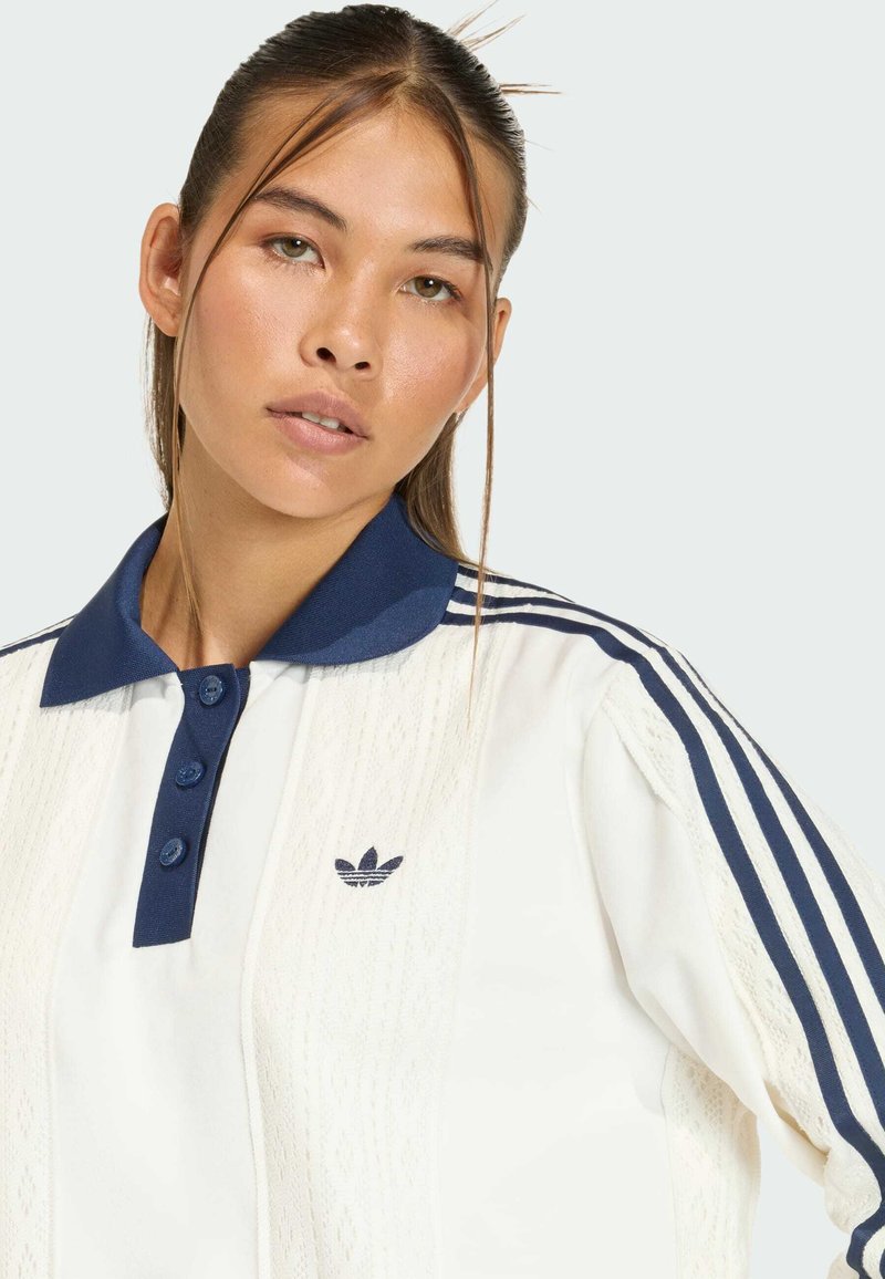 Hvid polo-shirt med detaljeret tekstur, navy krave og tre navy striber på ærmerne. Adidas-logoet er placeret på venstre bryst.