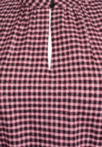 Czerwona i czarna bluzka w kratę z kołnierzykiem, z centralnym guzikiem i pionowym rozcięciem. Miękki materiał o lekko teksturowanej powierzchni.