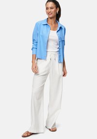 Light blue button-up shirt with long sleeves over a white sleeveless top, paired with white, high-waisted, wide-leg trousers and brown sandals.