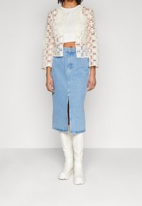 Vit blommig spetskort jacka över en vit topp, tillsammans med en knälång blå denimkjol med en framficka, och vita knähöga stövlar.