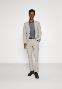 Lichtgrijs pak met een slim fit, gecombineerd met een donkergrijs overhemd met knopen. Zwarte leren schoenen complementeren de outfit. Soepele textuur, eenvoudig ontwerp.