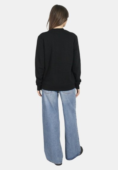 Maglione nero a maniche lunghe abbinato a jeans a gamba larga di un blu chiaro. Il maglione presenta un collo a giro e polsini a coste.
