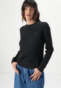 Pull en tricot noir avec motif texturé, col rond et poignets côtelés. Associé à un jean en denim bleu ample.
