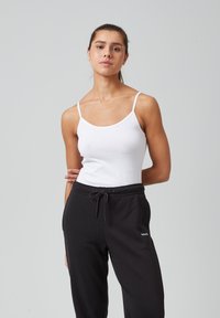 Witte katoenen tanktop met dunne bandjes, gecombineerd met zwarte sweatpants met een tailleband met trekkoord en een klein wit logo detail.