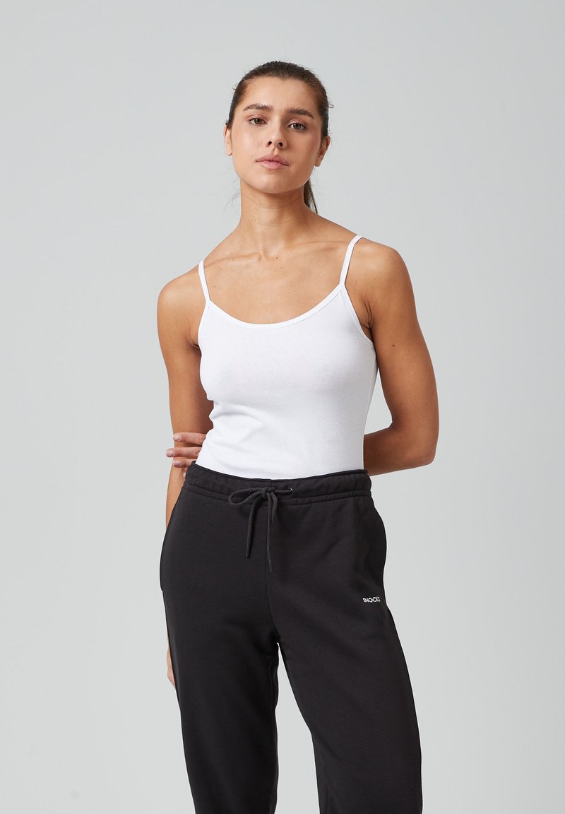 Witte katoenen tanktop met dunne bandjes, gecombineerd met zwarte sweatpants met een tailleband met trekkoord en een klein wit logo detail.