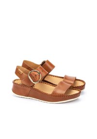 Sandalias de cuero marrón con dos correas anchas, una adornada con una hebilla metálica circular. Detalles de costura a lo largo de los bordes y una suela blanca.