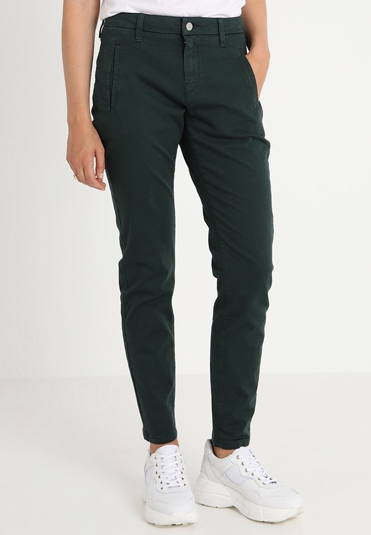Pantaloni attillati verde scuro in cotone misto con tasche laterali e passanti per cintura, abbinati a sneakers bianche con un design testurizzato.