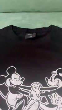 Camiseta negra con ilustración gráfica blanca de Mickey y Minnie Mouse cogidos de la mano. Tela suave, mangas cortas, cuello redondo.