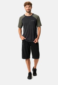 Camisa negra de manga corta con detalles en verde oscuro, combinada con pantalones cortos negros. La tela parece liviana y cómoda. Zapatillas negras completan el atuendo.