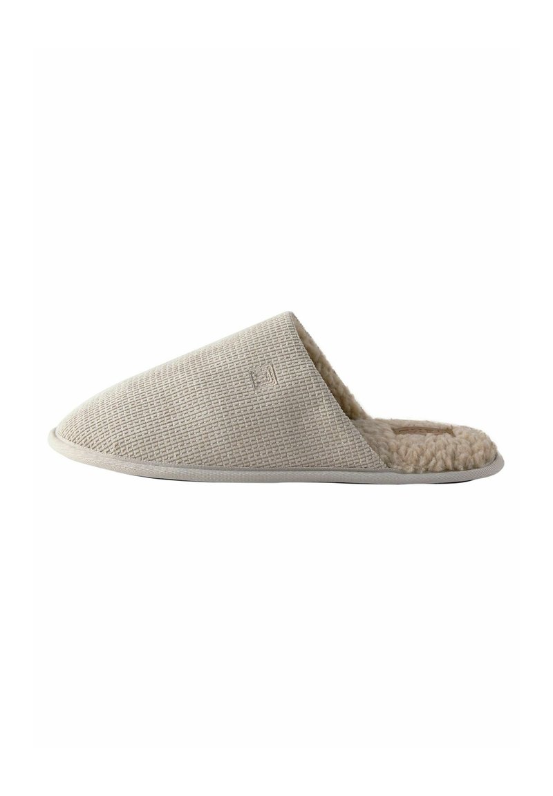 Beige Slipper ohne Schnürung mit strukturiertem, gewebtem Außenmaterial und weichem, flauschigem Innenfutter; runde Zehenform und flache Sohle.